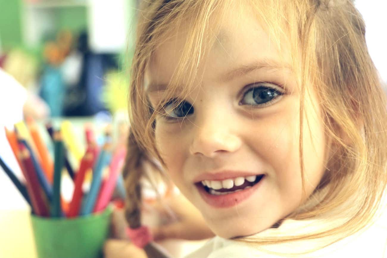 Una bambina sorride in classe, con i pastelli sul banco